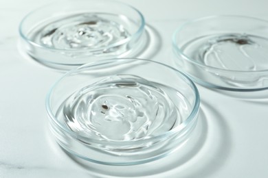 Photo of Petri dishes with liquids on white marble table, closeup