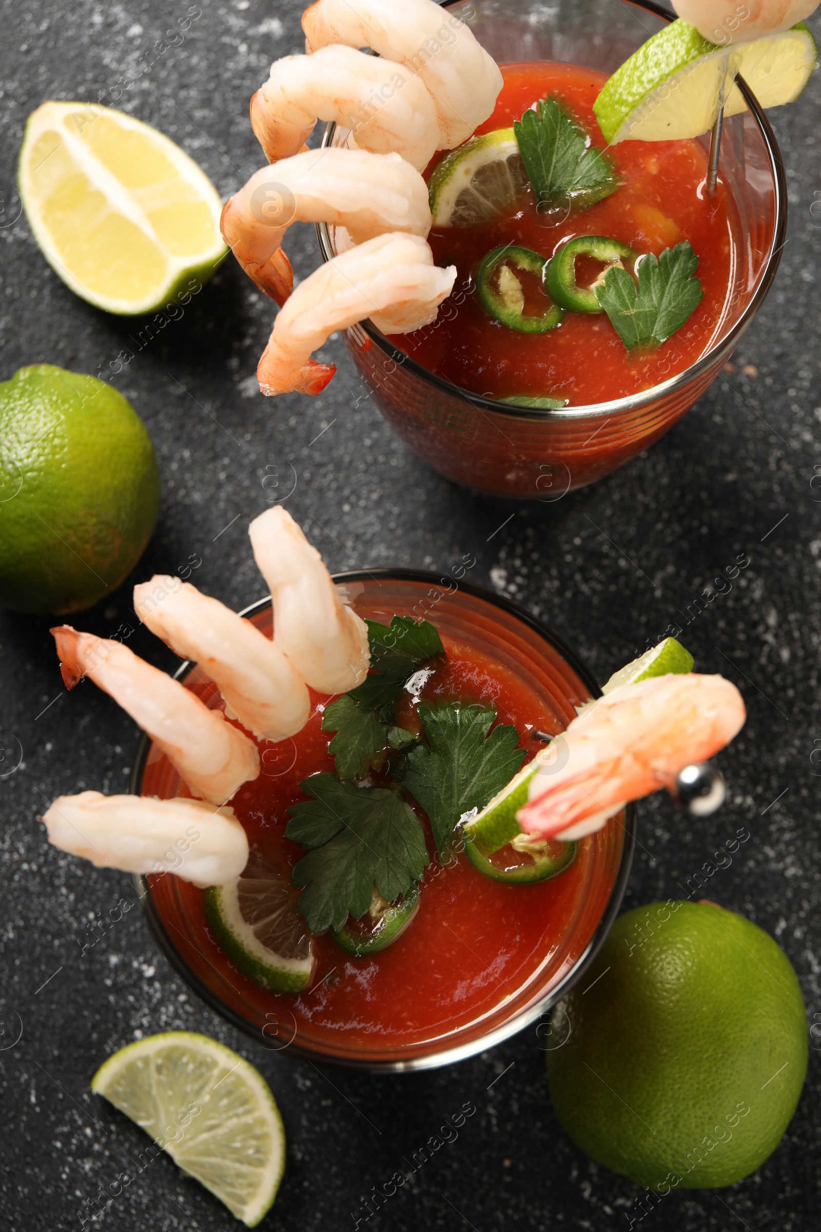 Photo of Tasty shrimp cocktail with sauce in glasses and limes on grey textured table, flat lay