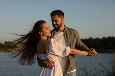 Beautiful couple dancing near river at sunset