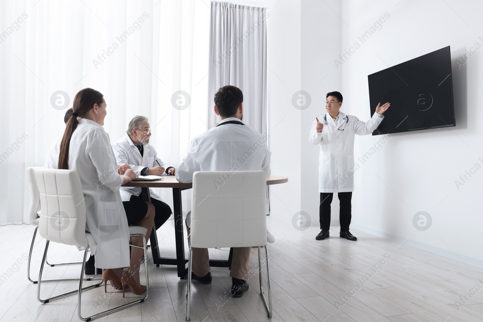 Photo of Team of doctors listening to speaker report near tv screen in meeting room. Medical conference