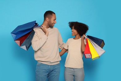 Photo of Happy African American couple with shopping bags on light blue background