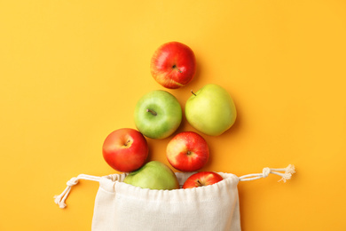 Photo of Cotton eco bag and apples on yellow background, flat lay