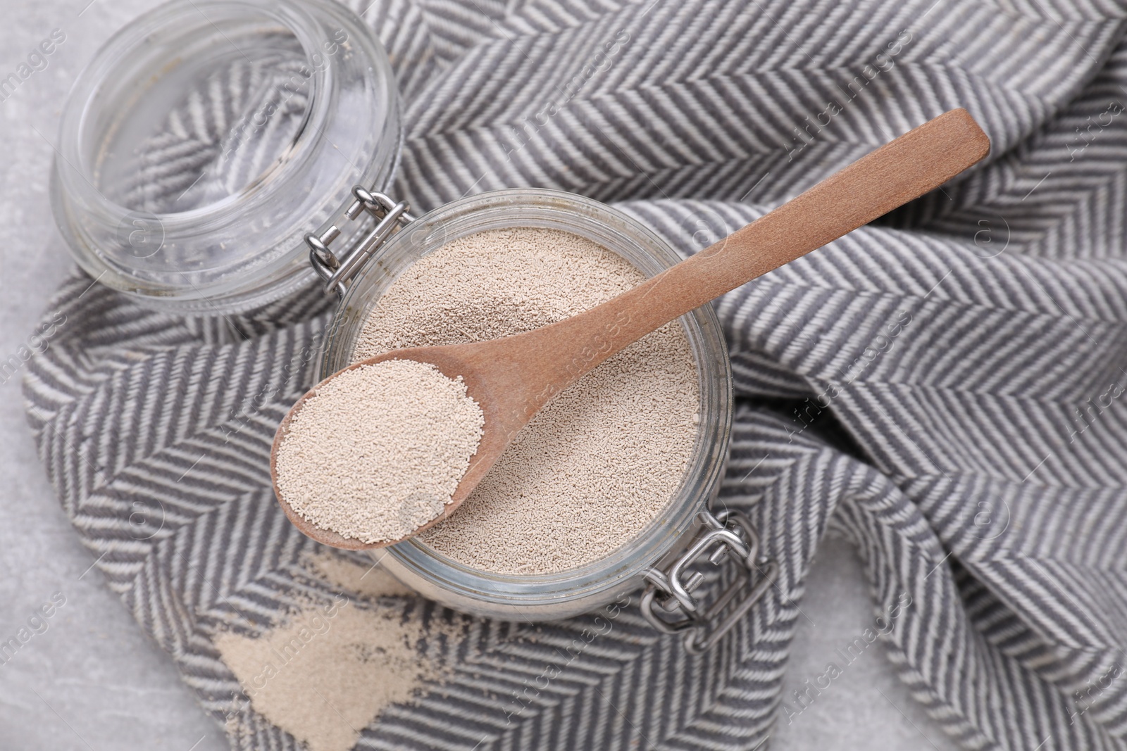 Photo of Glass jar and spoon with active dry yeast on light grey table, top view