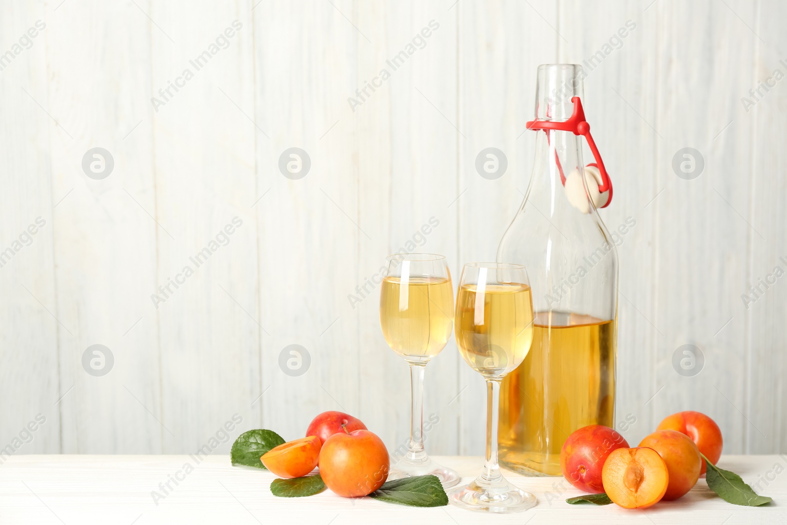 Photo of Delicious plum liquor and ripe fruits on white wooden table, space for text. Homemade strong alcoholic beverage