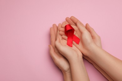 Woman and girl holding red ribbon on pink background, top view with space for text. AIDS disease awareness