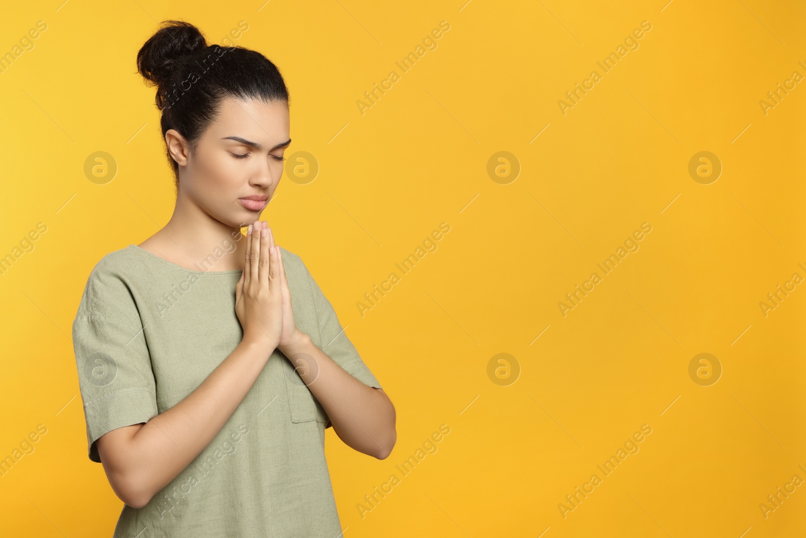 Photo of African American woman with clasped hands praying to God on orange background. Space for text