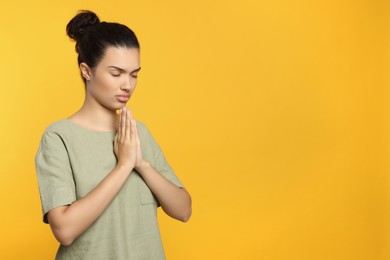 Photo of African American woman with clasped hands praying to God on orange background. Space for text