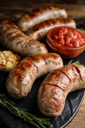 Photo of Tasty grilled sausages served with sauce on wooden table