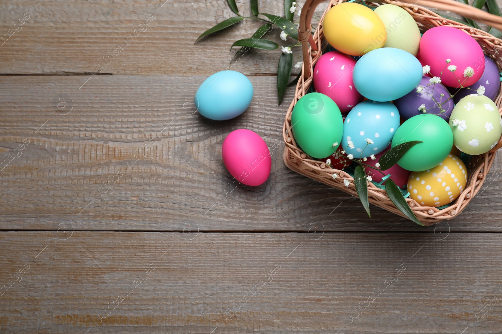 Photo of Colorful Easter eggs in wicker basket on wooden table, flat lay. Space for text