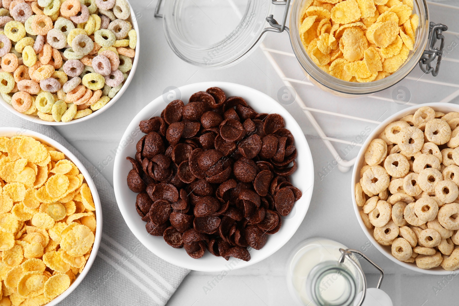 Photo of Different delicious breakfast cereals and milk on white tiled table, flat lay