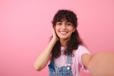 Beautiful woman taking selfie on pink background