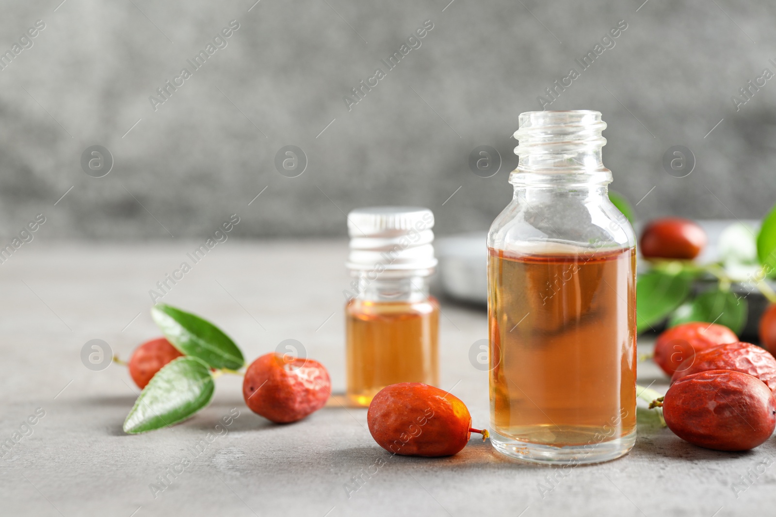 Photo of Glass bottle with jojoba oil and seeds on grey stone table. Space for text