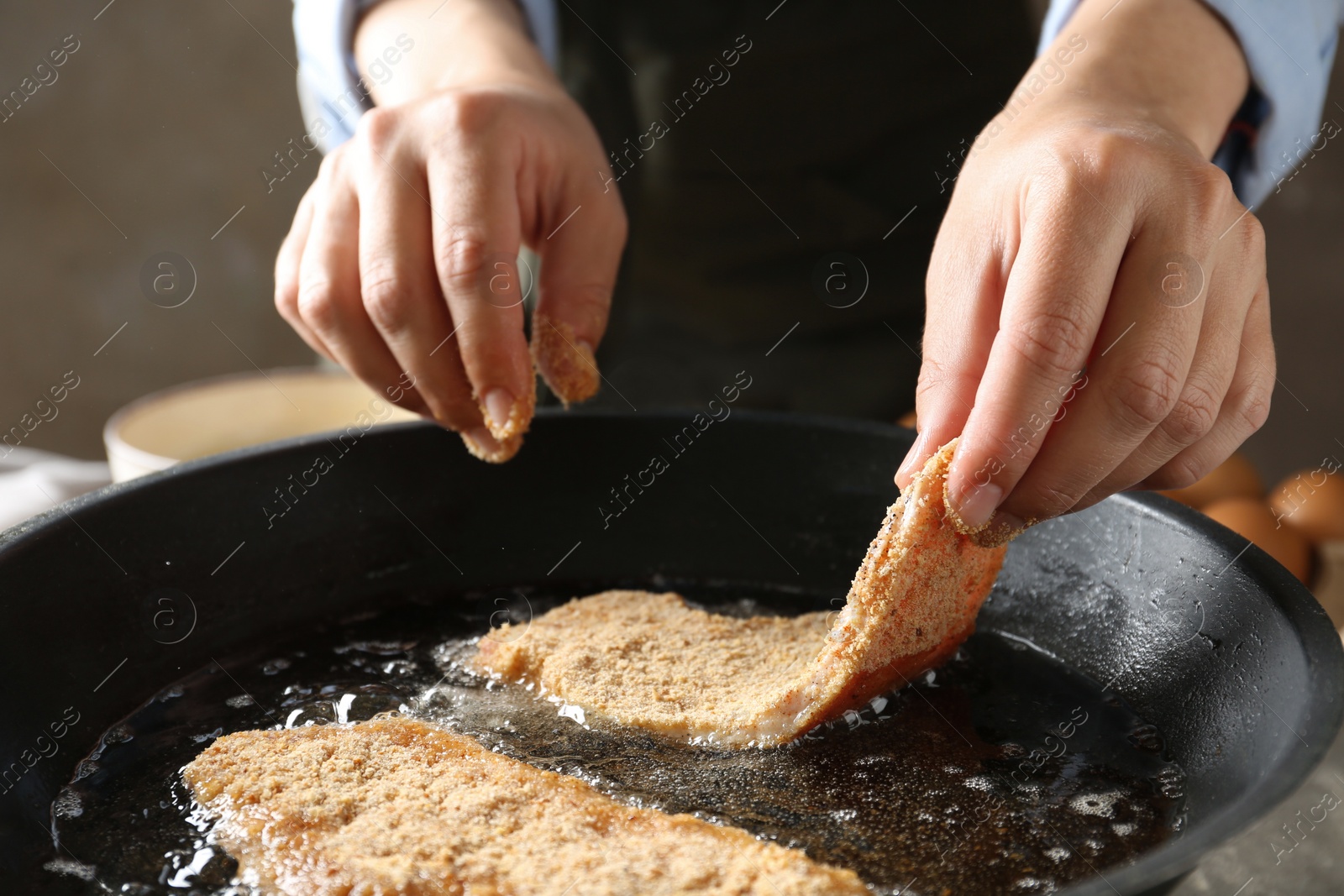 Photo of Cooking schnitzel. Woman putting raw pork chop in bread crumbs into frying pan, closeup