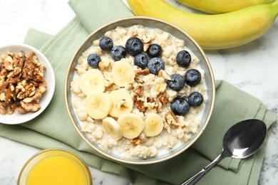 Tasty oatmeal with banana, blueberries, walnuts and milk served in bowl on white marble table, flat lay