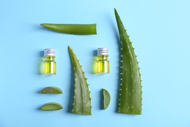 Photo of Bottles with aloe essential oil and fresh leaves on color background, flat lay