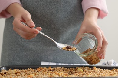 Photo of Woman putting granola from baking tray into jar at table, closeup