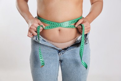 Photo of Woman in unfit jeans measuring her waist on light background, closeup. Weight loss concept