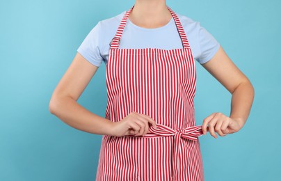 Woman in clean striped apron on light blue background, closeup