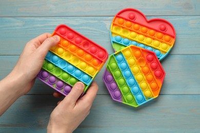 Photo of Woman using pop it fidget toy at light blue wooden table, top view