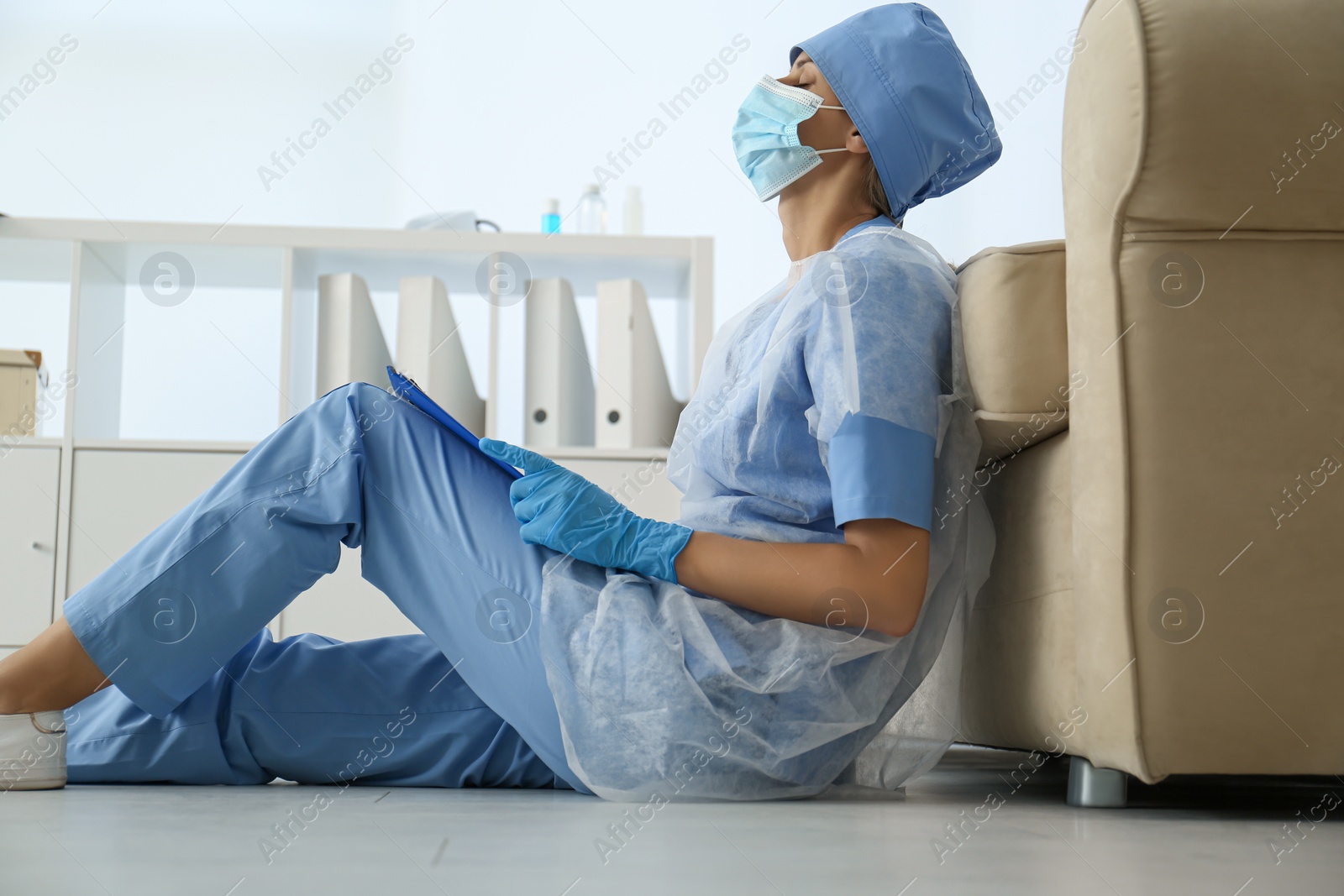 Photo of Exhausted doctor sitting on floor indoors. Stress of health care workers during COVID-19 pandemic