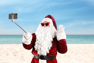 Image of Santa Claus in sunglasses taking selfie on beach near sea. Christmas vacation 