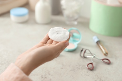 Photo of Young woman holding cotton pad with fallen eyelashes over table