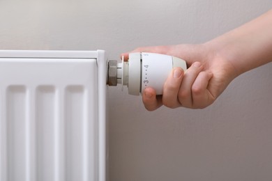 Photo of Girl adjusting heating radiator thermostat near white wall, closeup