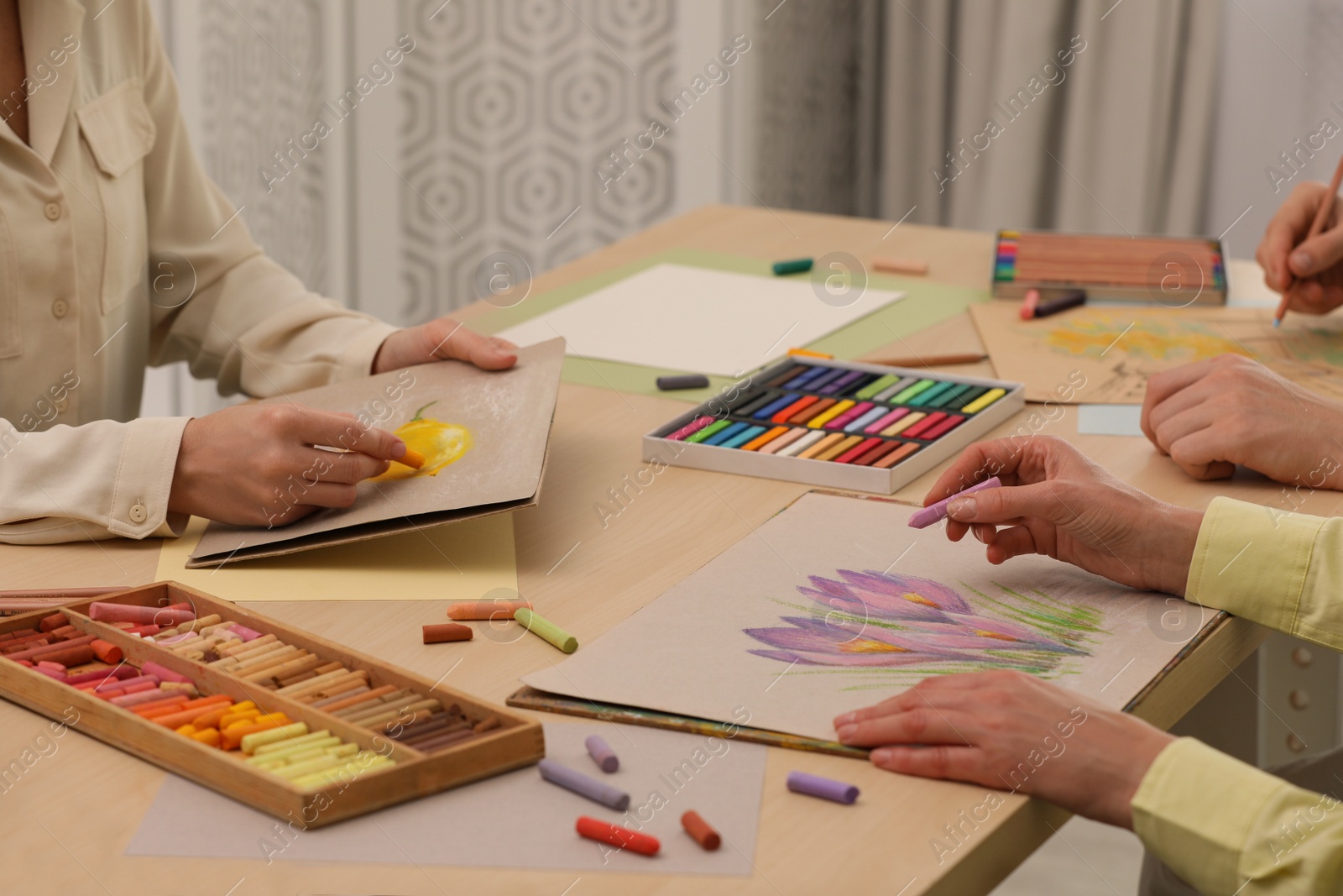 Photo of Artists drawing with soft pastels and pencils at table indoors, closeup