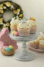 Photo of Tasty Easter cupcakes with vanilla cream and festive decor on light wooden table