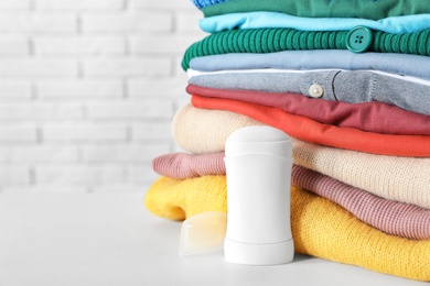 Photo of Stick deodorant near clean clothes on white table. Space for text