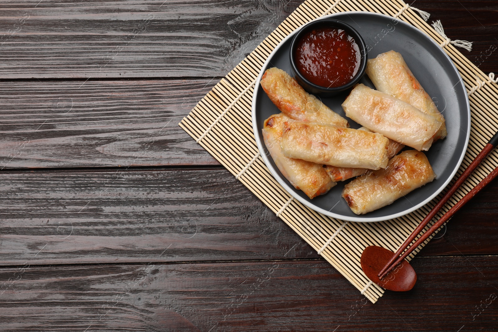 Photo of Tasty fried spring rolls and sauce served on wooden table, top view. Space for text