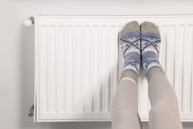 Photo of Woman warming feet near heating radiator, closeup. Space for text