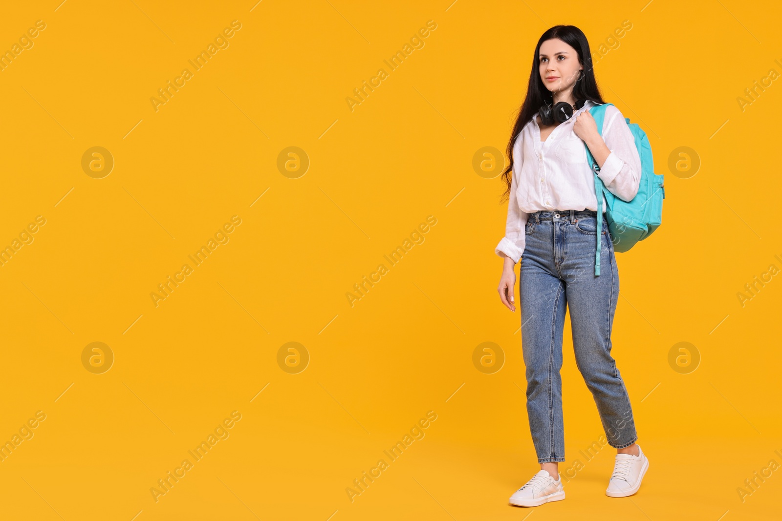 Photo of Student with backpack and headphones on yellow background. Space for text