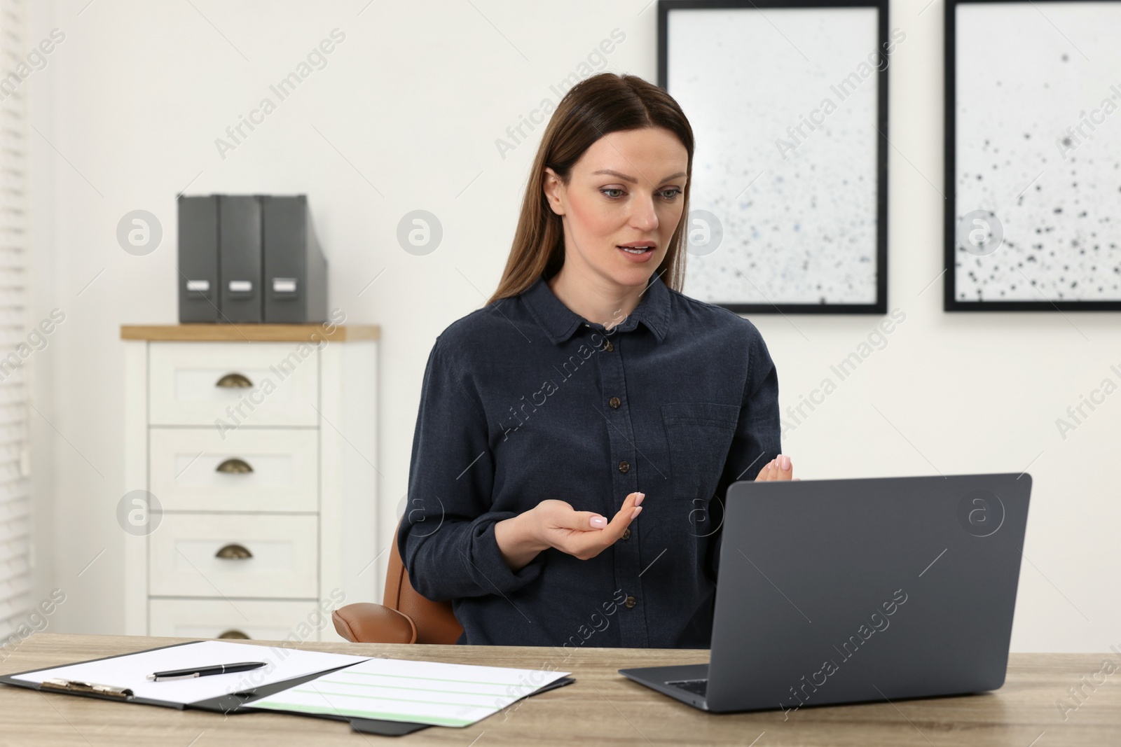 Photo of Woman having video chat via laptop at wooden table in office