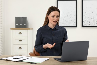 Woman having video chat via laptop at wooden table in office