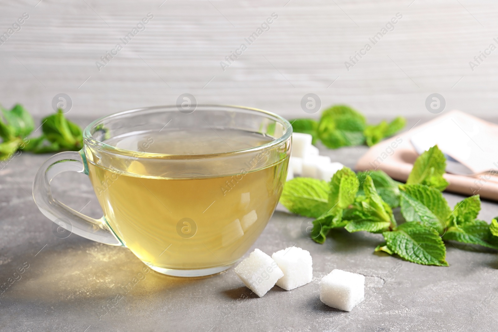 Photo of Cup with hot aromatic mint tea, fresh leaves and sugar cubes on table