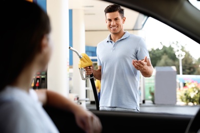 Photo of Man with fuel pump nozzle talking to his girlfriend at self service gas station