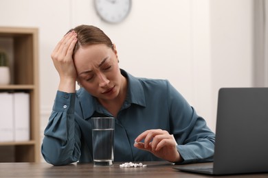Depressed woman with antidepressant pills and glass of water at wooden table indoors