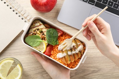 Woman eating healthy products high in vegetable fats near laptop at wooden table, top view