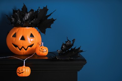 Jack-o'-lantern lights and black maple leaves on wooden fireplace near blue wall