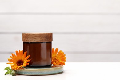 Photo of Jar of cosmetic product and beautiful calendula flowers on white table, space for text