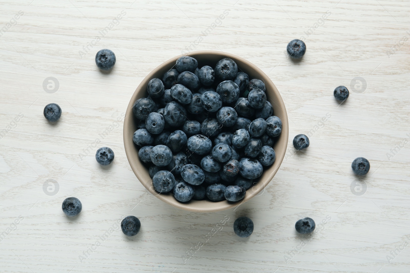 Photo of Ceramic bowl with blueberries on white wooden table, flat lay. Cooking utensil