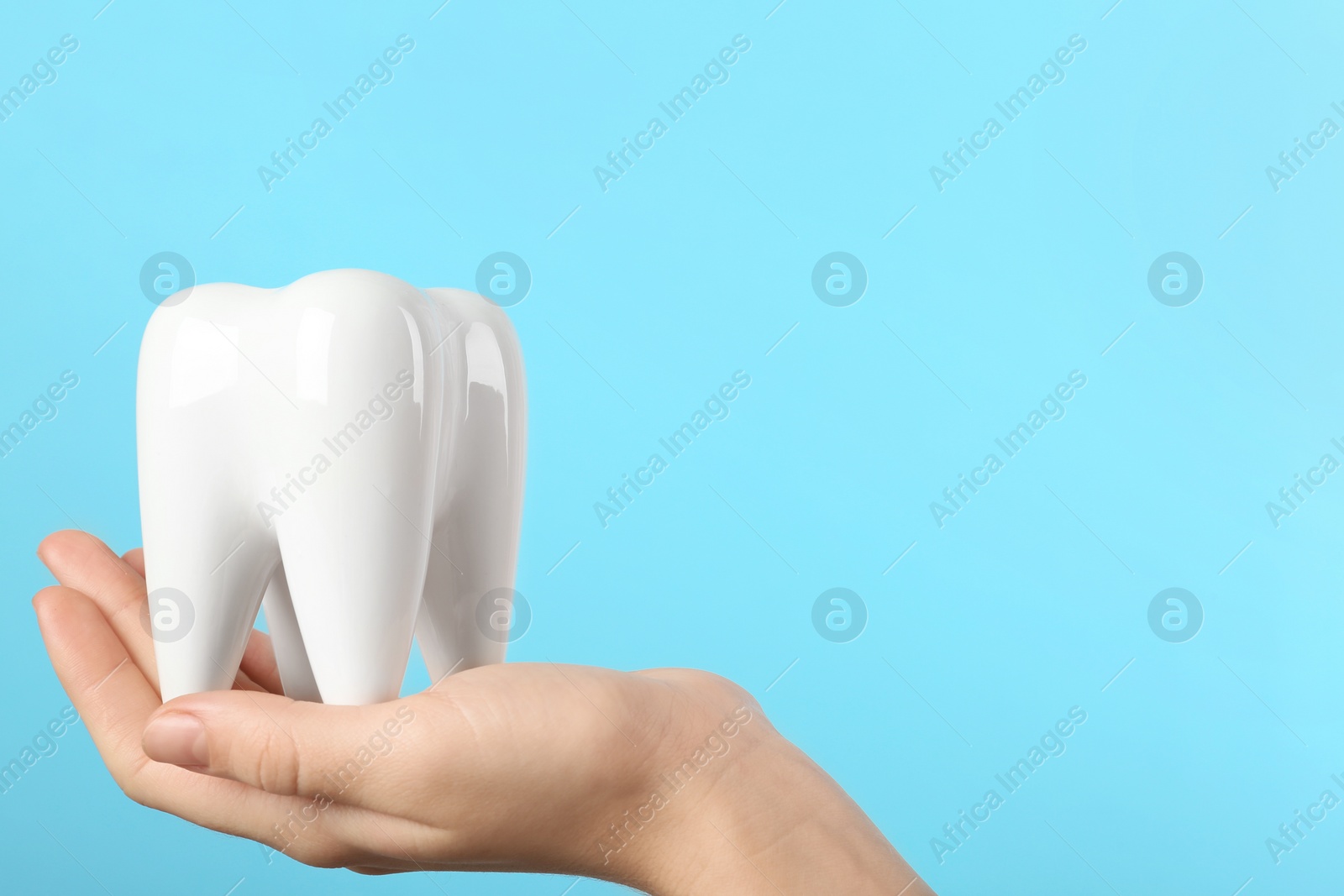 Photo of Woman holding ceramic model of tooth on color background, space for text