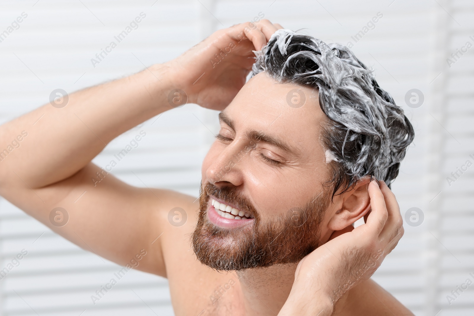 Photo of Happy man washing his hair with shampoo in shower