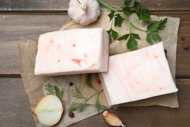 Tasty salt pork with herbs, onion and garlic on wooden table, flat lay