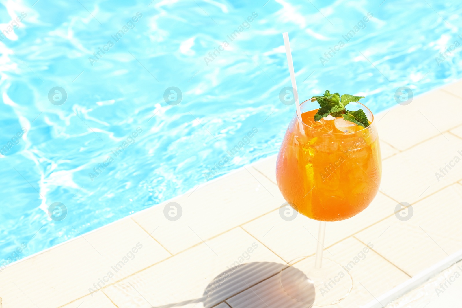 Photo of Glass of delicious cocktail near swimming pool, space for text. Refreshing drink