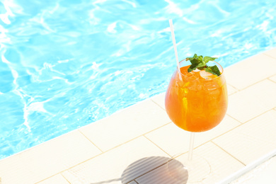 Photo of Glass of delicious cocktail near swimming pool, space for text. Refreshing drink