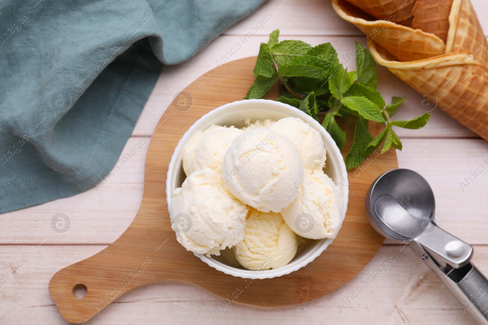 Photo of Bowl of ice cream, cones and mint leaves on light wooden table, flat lay