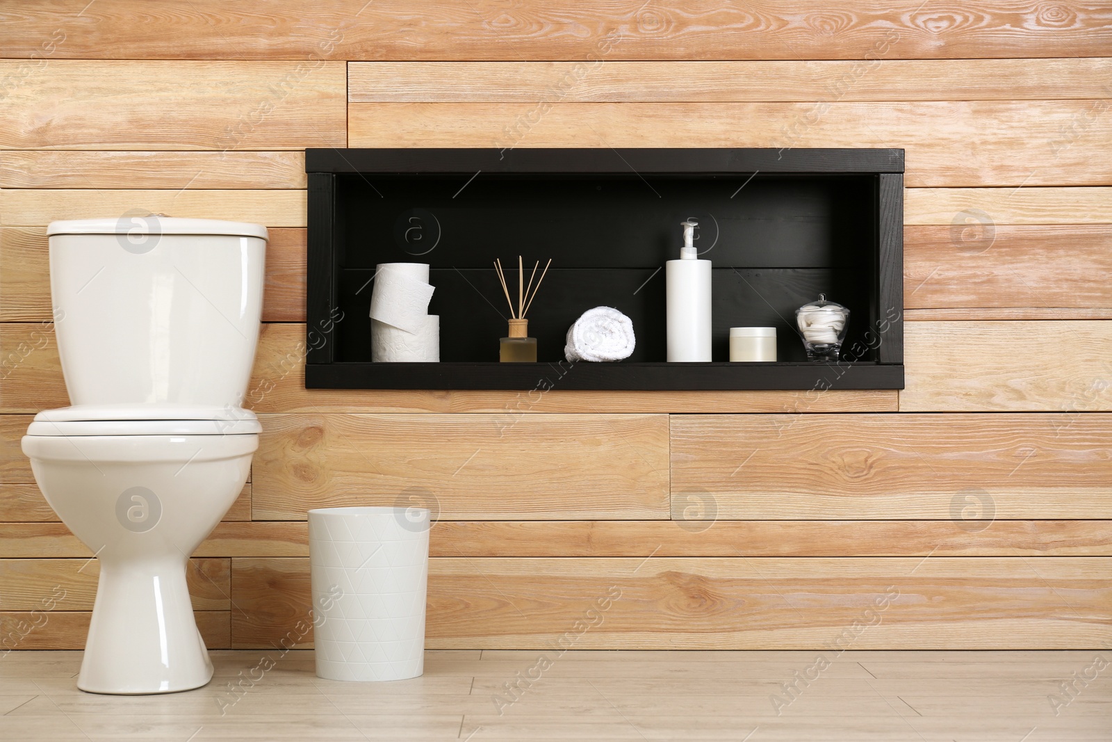 Photo of Toilet bowl at wooden wall with bathroom accessories in niche