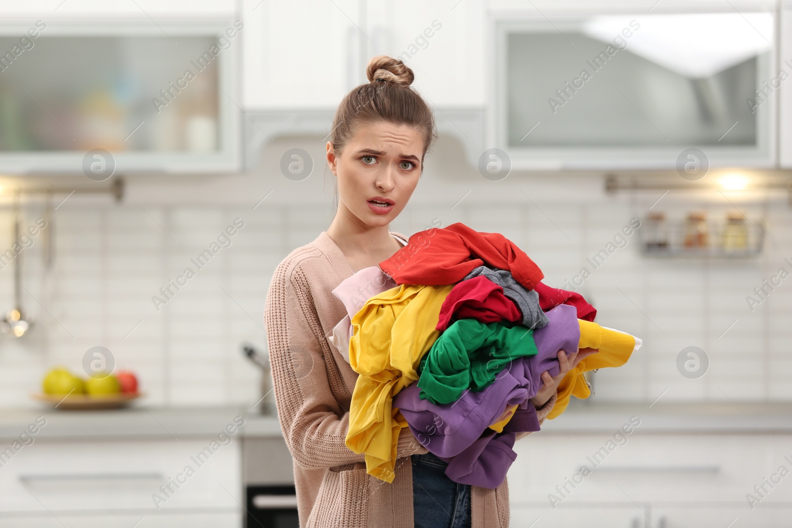 Photo of Woman holding pile of dirty laundry in kitchen